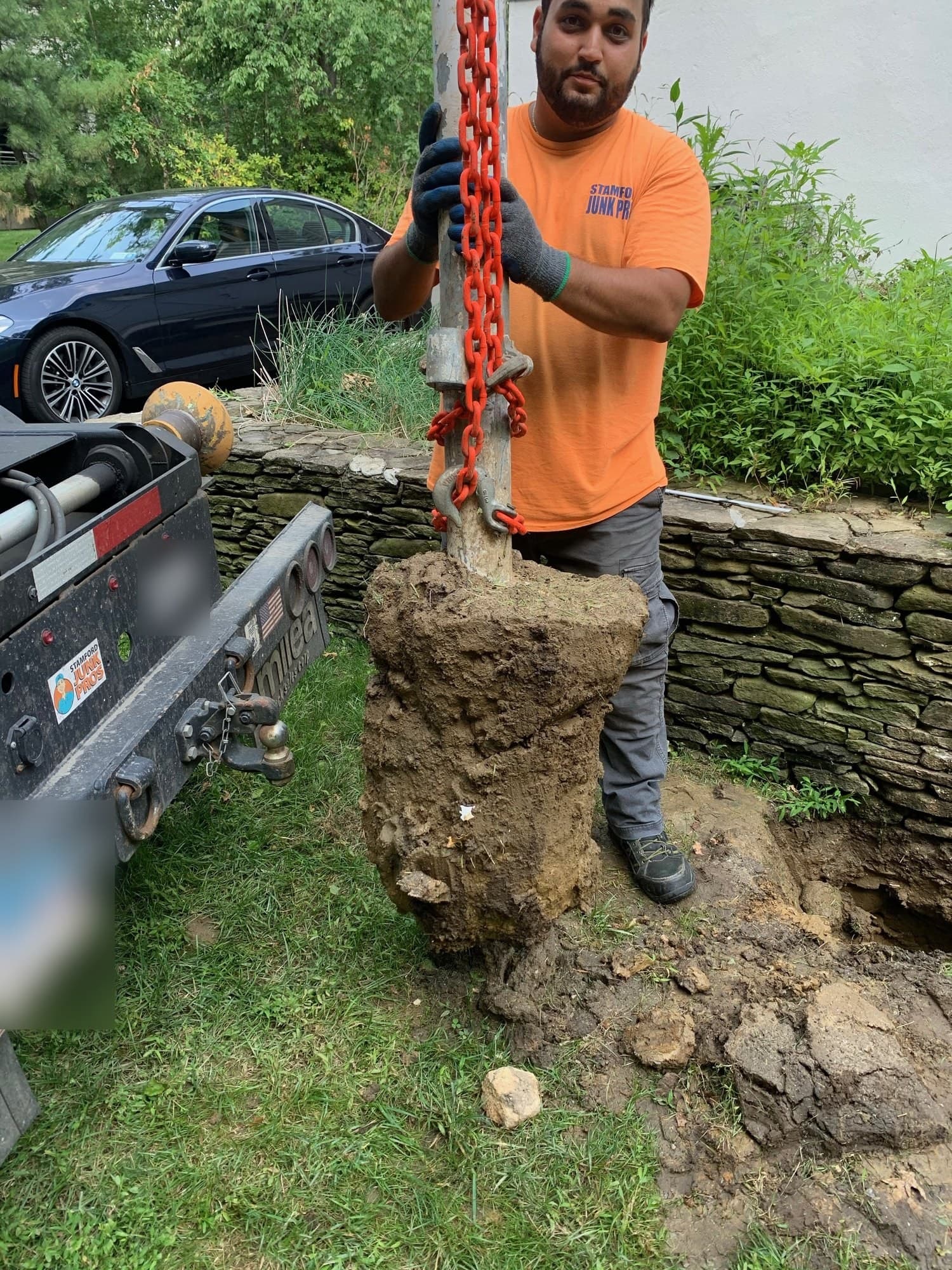 Crew member pulling a fence post and its concrete footing out on a chain