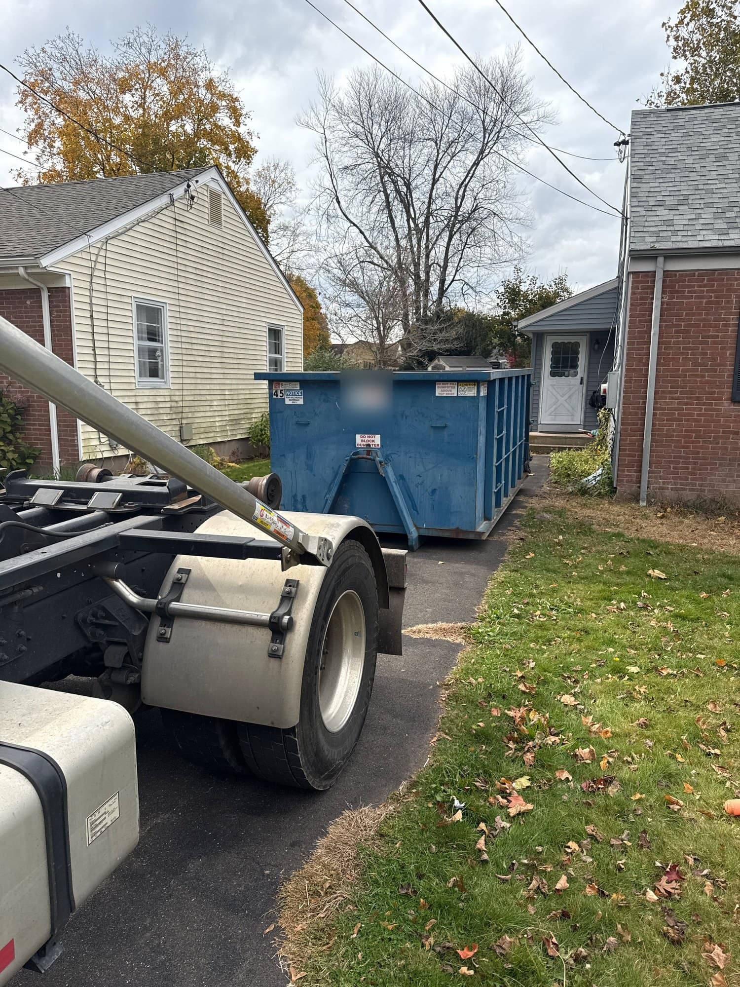 Blue roll-off dumpster in a driveway between two houses